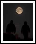 Two people on a walking trail at Signal Hill with the moon in the background